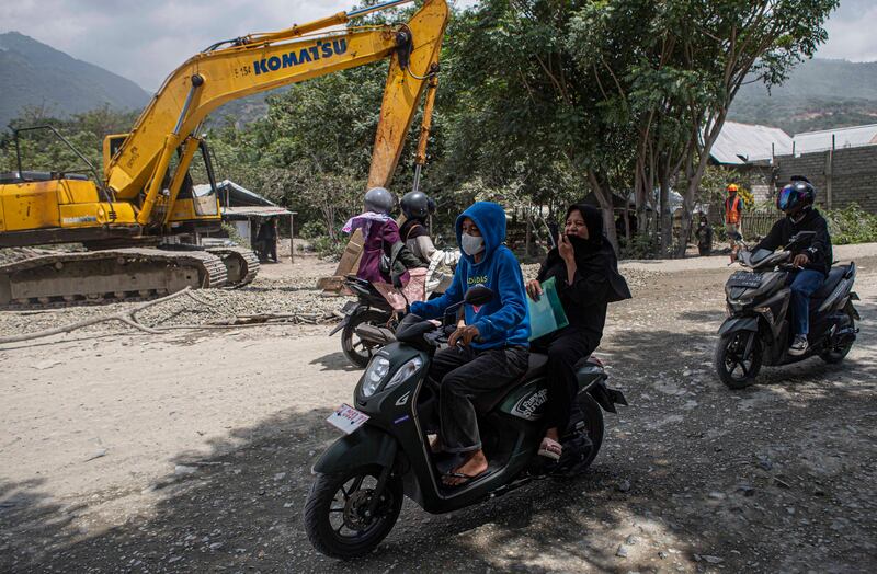 Pengendara sepeda motor menggunakan masker saat melintas di lingkar tambang galian C yang berdebu dengan alat berat di latar belakang, di Kelurahan Buluri, Palu, Sulawesi Tengah, 21 Mei 2024. [Taufan Bustan/BenarNews)