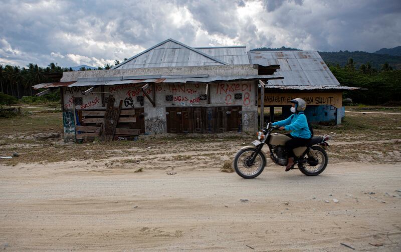 Warga mengendarai sepeda motor melintas di depan rumah yang tertimbun lumpur di Dusun 2, Desa Bangga, Kecamatan Dolo Selatan, Kabupaten Sigi, Sulawesi Tengah, Minggu [15/1/2023). Pemerintah desa bersama pemerintah kabupaten berencana merevitalisasi perkampungan bekas bencana alam ini dengan menjadikan pusat ekonomi baru dan obyek wisata. Di mana, sepanjang jalan poros Bangga – Pakuli, sebuah desa lainnya di Sigi ini akan dibangun pusat jajanan rakyat seusai pengaspalan kembali dilakukan. [Taufan Bustan/BenarNews]