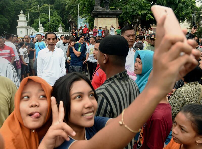 Dua perempuan melakukan swafoto dengan latar belakang Presiden Joko “Jokowi” Widodo di Jakarta, 24 Januari 2016. (Dok. Istana Kepresidenan/AFP)