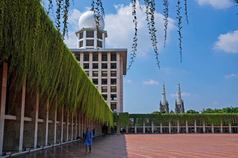 Seorang laki-laki berjalan di pelataran Masjid Istiqlal sementara menara Gereja Katedral Santa Maria Diangkat ke Surga terlihat di latar belakang, di Jakarta, Jumat, 9 Agustus 2024. [Tatan Syuflana/AP]