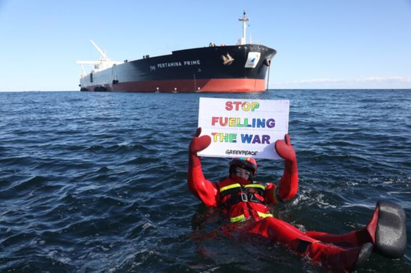 Seorang aktivis Greenpeace memegang plakat anti-perang di depan supertanker Pertamina Prime di lepas pantai Denmark pada 31 Maret 2022, mengecam pengiriman minyak Rusia yang ada dalam kapal tersebut. [Greenpeace via AFP]