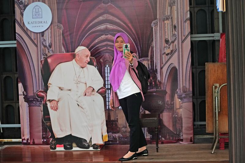 Seorang perempuan berswafoto dengan potongan gambar pemimpin agama Katolik Paus Fransiskus di Gereja Katedral Santa Maria Diangkat ke Surga, atau Katedral Jakarta, di Jakarta, 8 Agustus 2024. [Achmad Ibrahim/AP]