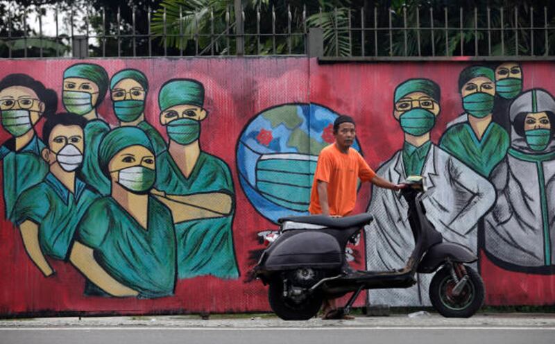 Dalam foto tertanggal 15 April 2020 ini, seorang lelaki dengan kendaraan bermotornya berdiri di depan sebuah mural yang dibuat untuk menghormati para tenaga kesehatan yang telah banyak berjatuhan dalam penanganan pandemi COVID-19. (AP)