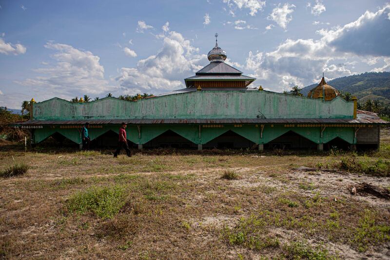 Dua warga berjalan di depan masjid Bangga yang tertimbun lumpur kering di Dusun 2, Desa Bangga, Kecamatan Dolo Selatan, Kabupaten Sigi, Sulawesi Tengah, 15 Januari 2023. Bangunan masjid yang tersisa ini rencananya tahun ini akan dirobohkan lalu didiirikan kembali oleh pemerintah desa sehingga bisa dioperasikan lagi sebagai tempat ibadah. [Taufan Bustan/BenarNews]