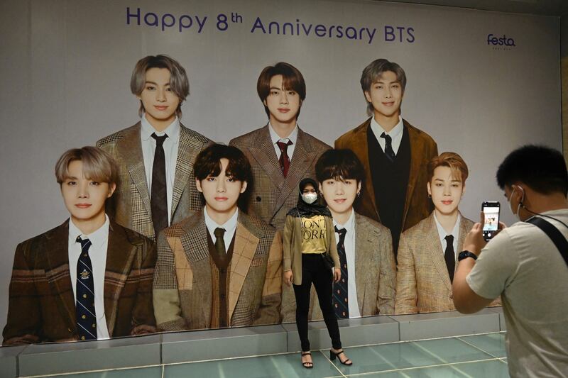 Seorang penggemar K-pop BTS berpose dengan poster raksasa anggota band tersebut di sebuah pusat perbelanjaan di Jakarta pada 21 Juni 2021. [Goh Chai Hin/AFP]