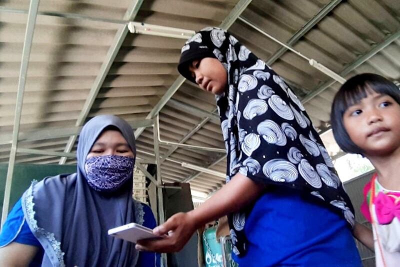 Koreeyoh Samae (right) helps Rokeeyoh Abu check if money from government aid was transferred to her bank account, in Yala, Thailand, April 8, 2020. [BenarNews]