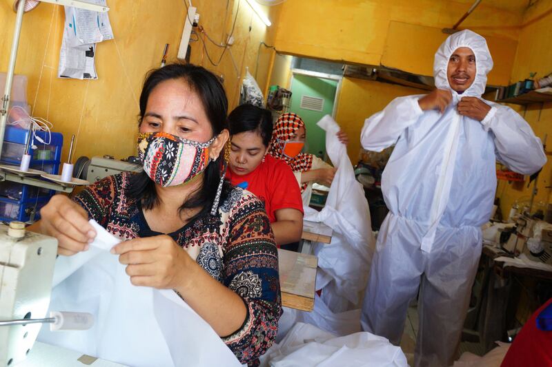 Sejumlah karyawan (kiri) memproduksi pakaian pelindung dari virus corona COVID-19, sementara seorang pria (kanan) mengenakan pakaian tersebut di sebuah industri kecil di Tangerang, Banten, 2 April 2020. [Fajrin Raharjo/AFP]