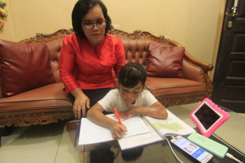 Sarina Gultom menemani putrinya, Trinity Hutahean (7), mengerjakan tugas sekolahnya, di rumahnya di Samarinda, Minggu (11/10/2020).“Saya minta Trinity menutupi kekurangan fisik dengan kemampuan akademis,” ujar sang Ibu. [BenarNews]