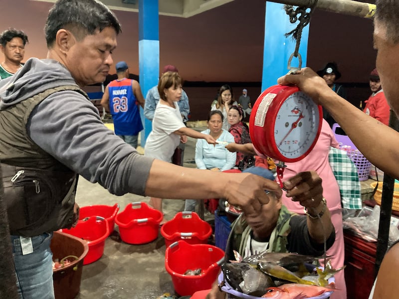 A fisherman weighs his catch at the market in Masinloc, Feb. 27, 2024. (Jojo Riñoza/BenarNews)