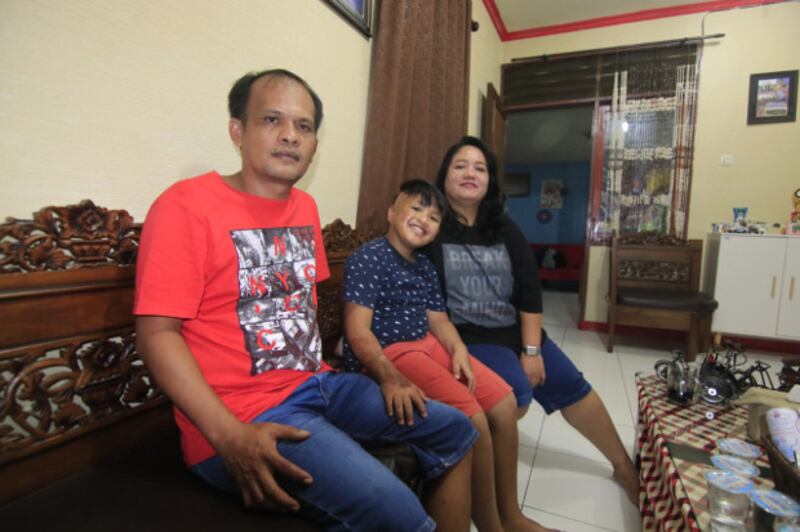Alvaro Aurelius Tristan Sinaga (8) tampak gembira duduk diapit kedua orangtuanya di rumah mereka di Samarinda, Minggu, 11 Oktober 2020. [BenarNews]
