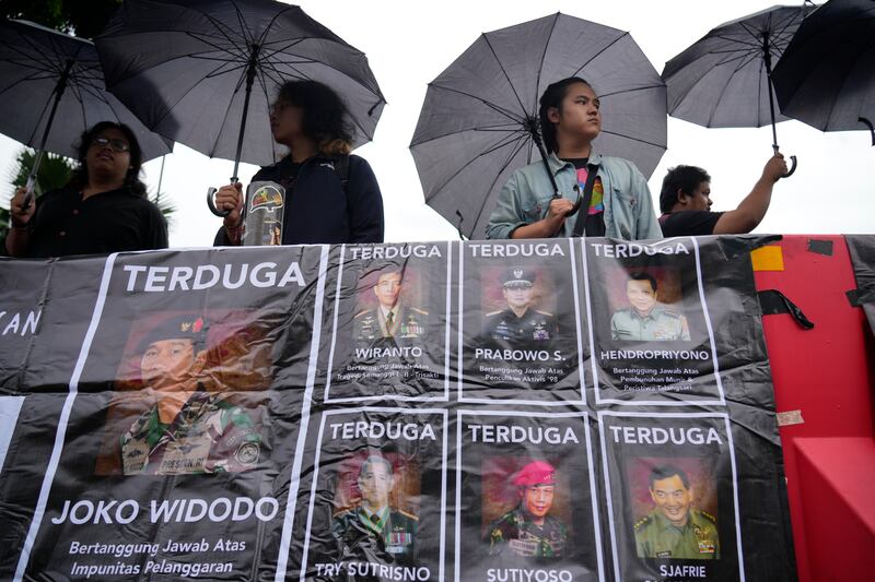 Para aktivis memegang payung sambil memajang spanduk bergambar para jenderal Angkatan Darat yang mereka tuduh melakukan pelanggaran hak asasi manusia di masa lalu, termasuk Menteri Pertahanan dan presiden terpilih Prabowo Subianto (tengah atas) dalam “Aksi Kamisan", protes mingguan yang diadakan oleh keluarga korban pelanggaran hak asasi manusia di Indonesia, di luar Istana Merdeka di Jakarta, Kamis, 29 Februari 2024. [Achmad Ibrahim/AP]