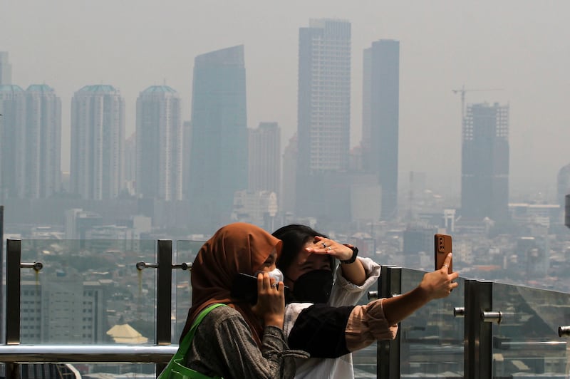 Dua perempuan berswafoto di gedung tinggi dengan latar belakang langit kota Jakarta yang terlihat kelabu karena polusi udara, Kamis, 10 Agusts 2023. [Eko Siswono Toyudho/BenarNews]