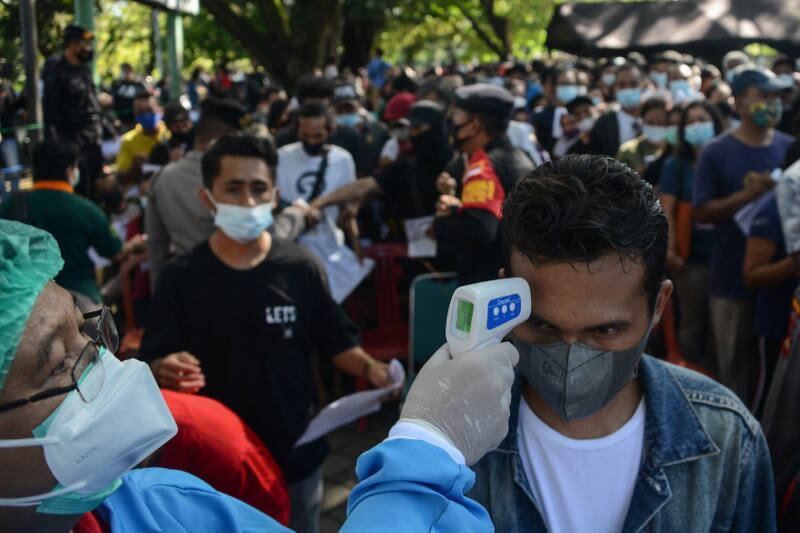 Seorang petugas kesehatan mengecek suhu salah seorang warga yang antri untuk mendapatkan vaksinasi COVID-19 AstraZeneca di Denpasar, 26 Juni 2021. [AFP]