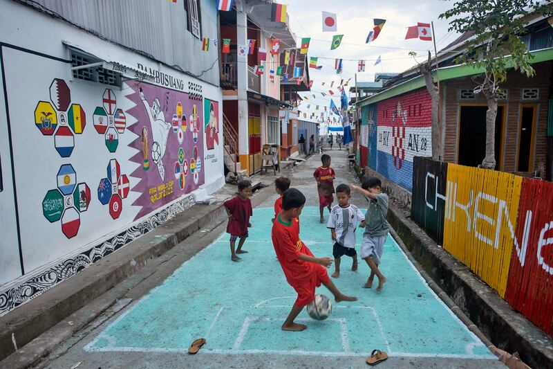 Anak-anak bermain sepak bola di gang di dekat tempat tinggal mereka yang dihiasi mural bertemakan Piala Dunia 2022 di desa Pambusuang, Sulawesi Barat, 20 November 2022. [Yusuf Wahil/AP Photo]