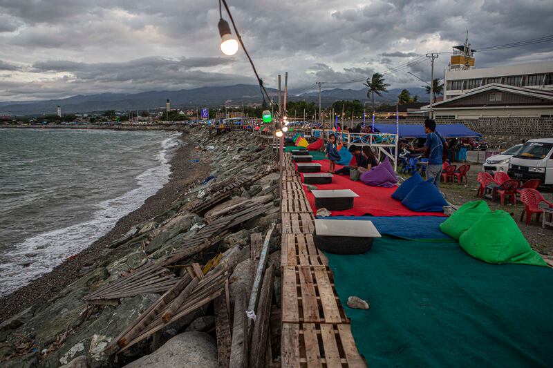 Seorang pengamen menghibur pengunjung yang datang bersantai di kafe milik penyintas gempabumi dan tsunami yang dibangun di atas tanggul Teluk Palu di pantai talise, Palu, Sulawesi Tengah, Rabu, 15 Februari 2023. Kafe sepanjang Pantai Talise dihias sedemikian rupa demi menarik pengunjung untuk datang. Beberapa asesoris yang dipasang seperti bantal duduk, karpet, dan lampu semuanya berwarna-warni. Asesoris ini menjadi salah satu daya tarik yang berhasil mendatangkan pengunjung selain pesona pantai yang indah. [Taufan Bustan/BenarNews]