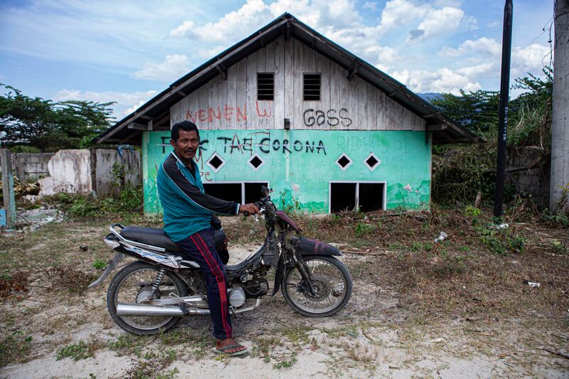 Arifin, seorang warga setempat, duduk di atas sepeda motor dengan latar belakang rumahnya yang menyisakan setengah bangunan akibat terkubur material banjir berupa lumpur bercampur pasir yang telah mengering di Dusun 2, Desa Bangga, Kecamatan Dolo Selatan, Kabupaten Sigi, Sulawesi Tengah, 15 Januari 2023. Sebanyak 590 rumah warga dengan rincian 300 rumah di Dusun 1 dan 290 rumah di Dusun 2 terkubur pasca banjir bandang yang terjadi pada 2019. Dalam musibah itu, satu korban meninggal dunia. [Taufan Bustan/BenarNews]