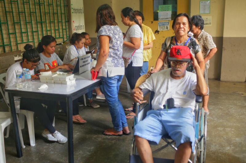 A woman helps a man in a wheelchair after he cast his ballot at a Manila polling precinct, May 13, 2019. [Luis Liwanag/BenarNews]