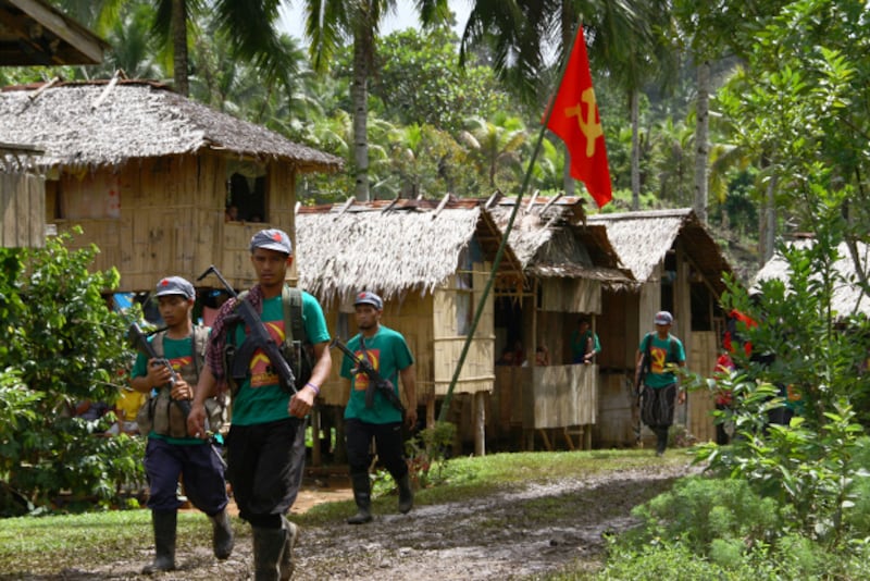 Members of the New People's Army, armed wing of the Communist Party of the Philippines, walk past a hammer-and-sickle flag displayed in a village on the southern island of Mindanao, Dec.26, 2014. [AFP]