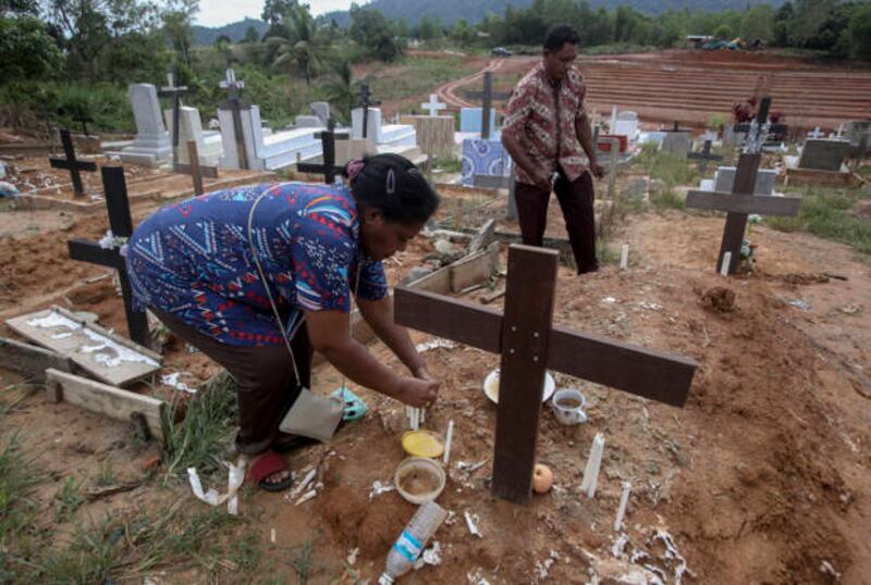 Seorang pekerja migran Indonesia meletakkan lilin di atas makam suaminya yang bekerja di perkebunan kelapa sawit di Sabah, Malaysia, 9 Desember 2018. Jenazah buruh migran yang meninggal terkadang tidak dikirim kembali ke Indonesia. (AP)