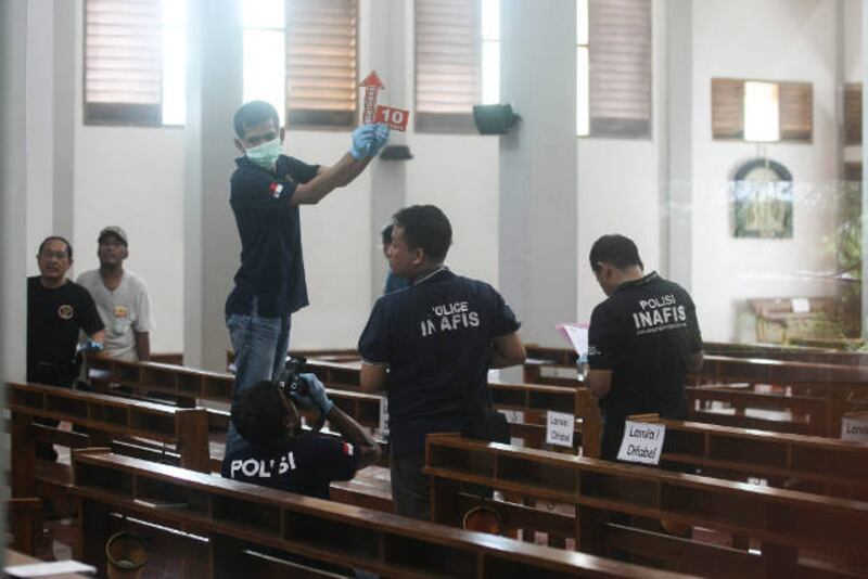 In this photograph shot through a glass window, police investigators examine the interior of St. Lidwina Church in Yogyakarta province, Indonesia, following an attack by a sword-wielding man during Sunday Mass, Feb. 11, 2018.