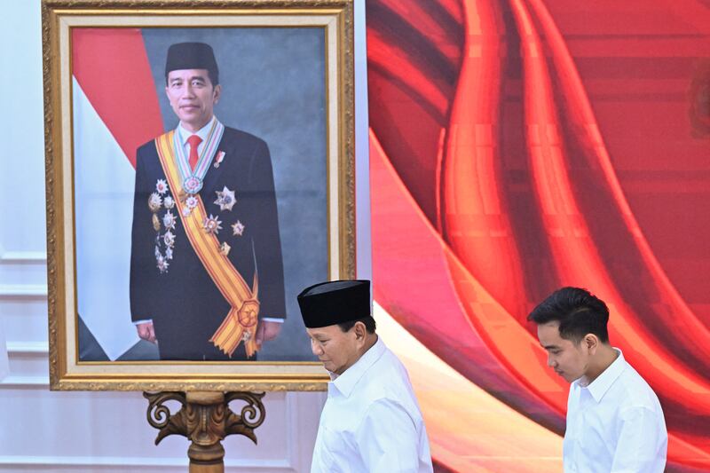 Presiden terpilih, Menteri Pertahanan Prabowo Subianto (kiri), dan wakil presiden terpilih, Wali Kota Solo Gibran Rakabuming Raka (kanan), berjalan melewati foto Presiden Indonesia Joko Widodo, ayah dari Gibran, saat rapat pleno Komisi Pemilihan Umum yang mengumumkan hasil Pemilihan Presiden 2024 di Jakarta pada 24 April 2024. [Adek Berry/AFP]