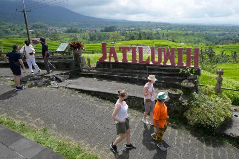 Wisatawan berjalan di dekat sawah yang diairi oleh sistem irigasi tradisional yang disebut “subak” di Bali, 18 April 2022. [Tatan Syuflana/AP]