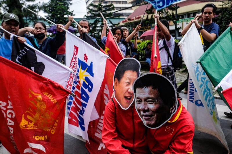 Members of the indigenous rights group Cordillera People's Alliance carry flags pointed at their fellow demonstrators wearing Duterte and Xi masks during a protest rally in the northern Philippine city of Baguio, July 22, 2019. [Jojo Rinoza/BenarNews]