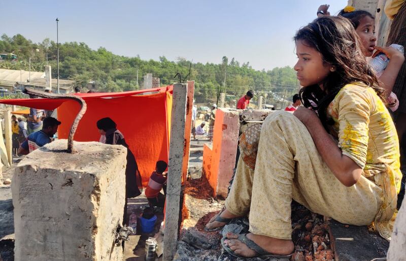 কক্সবাজার উখিয়ার পালংখালীর ১৬ নম্বর শরণার্থী শিবিরে আগুনে পোড়া ভিটায় বসে আছে এক রোহিঙ্গা কিশোরী। ১০ জানুয়ারি ২০২২। [আবদুর রহমান/বেনারনিউজ]