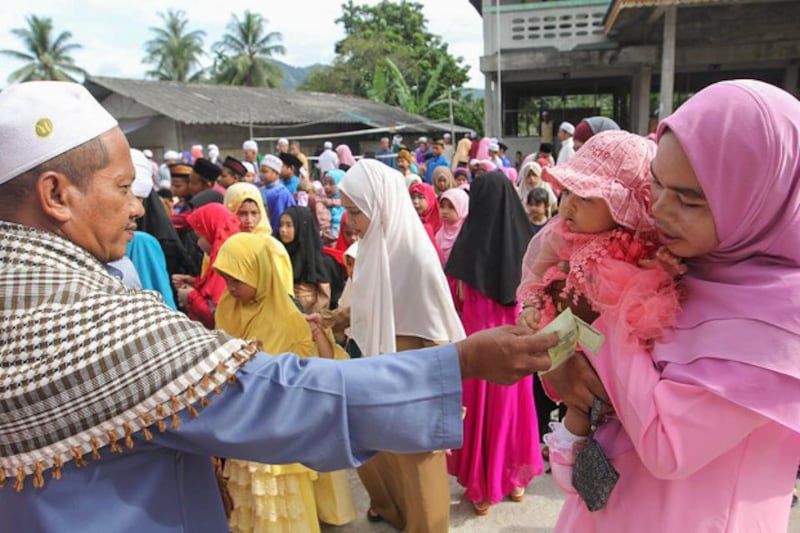 A man hands out cash to a child and mother on Raya Adha day at a mosque in Yaha, a district of the southern Thai province of Yala, Aug. 22, 2018 (Mariyam Ahmad/BenarNews)