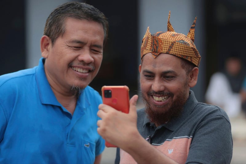 Militan JI Umar Patek (kanan) menggunakan ponselnya untuk melakukan panggilan video saat bertemu dengan teman lamanya Ali Fauzi, mantan pembuat bom yang menjalankan program untuk menderadikalisasi militan, di Lamongan, Jawa Timur, 13 Desember 2022. [Trisnadi/AP]